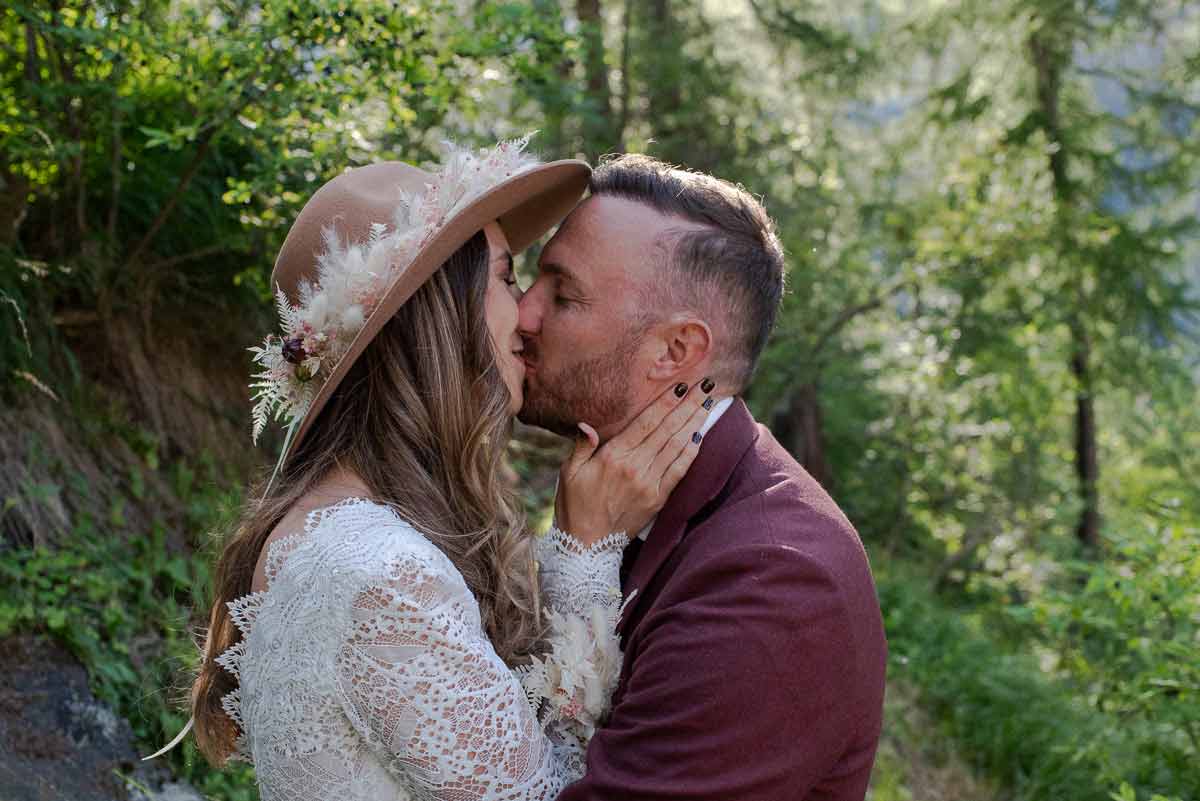 Boho-Brautpar steht eng umschlungen im wald und küsst sich.