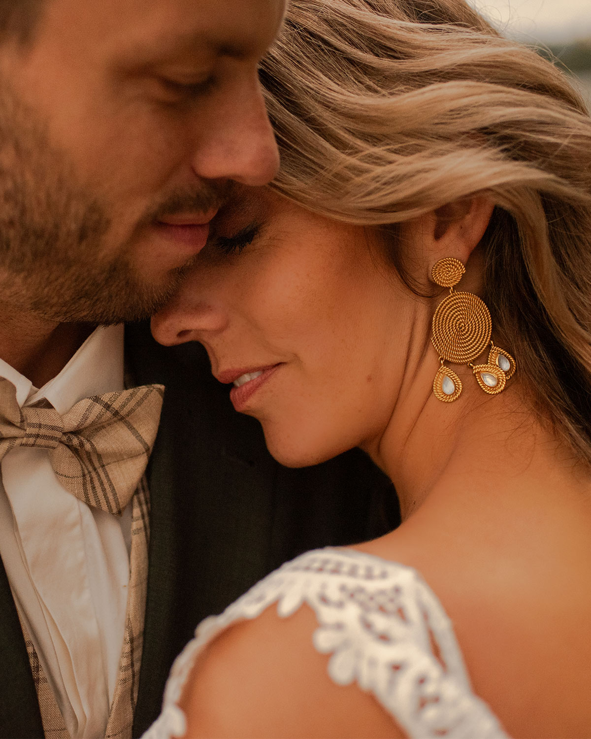 Brautpaar Wange an Wange im warmen Abendlicht, die Braut mit Spitzenkleid und goldenen Ohrringen – Hochzeitsfotograf Roman Schaller
